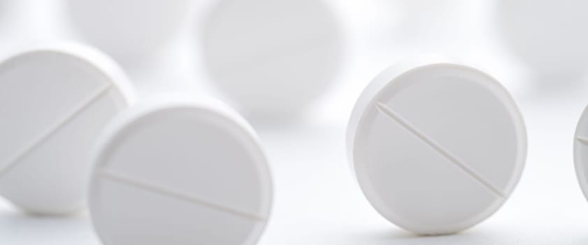A pile of white pills scattered on a bright white background. Selective focus. Mockup layout, template.