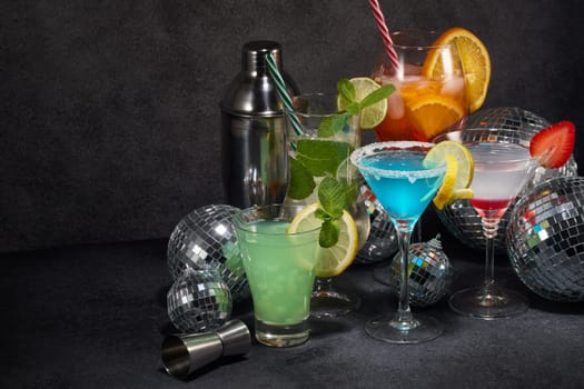 Cocktails set and disco balls. Glasses with various cold bright beverages, mirror balls and  bar tools on dark gray background. Nightclub. Weekend or holiday party. New Year and Christmas