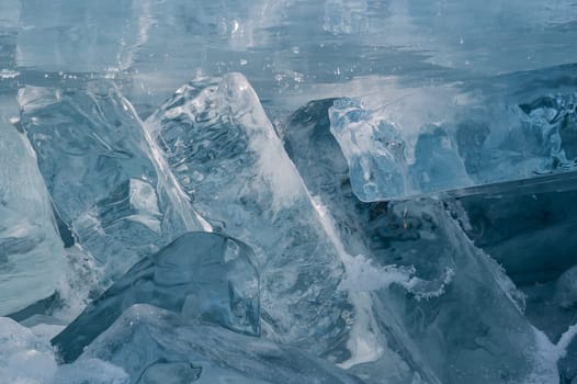Transparent blue ice floes piled in ice hummocks against a blue sky on a sunny day. Unusual winter landscape of the frozen lake Baikal. Natural cold background. Siberia, Russia.