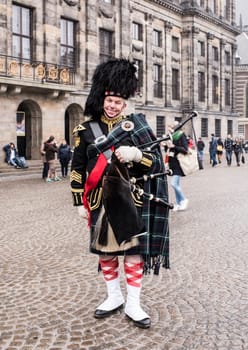 Amsterdam,Netherlands-December 30,2016:Bagpiper with his bagpipe in the square. Nearby are walking tourists
