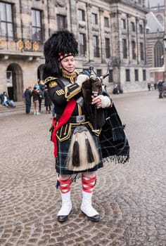 Amsterdam,Netherlands-December 30,2016:Bagpiper with his bagpipe in the square. Nearby are walking tourists