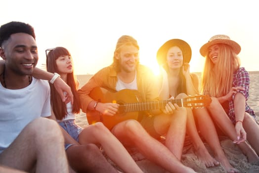 Happy group of friend having party and playing guitar on the beach