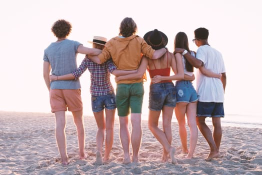 Group of happy friends having fun at ocean beach at dawn