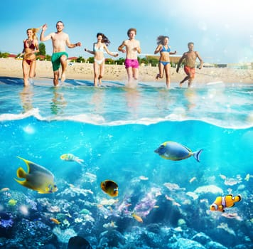 Group of friends run to the crystalline sea with colorful fishes. Concept of summertime