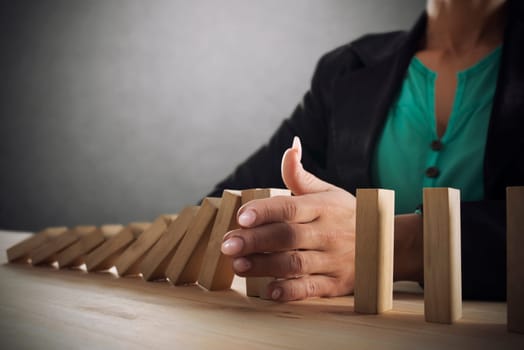 Businesswoman stops a chain fall like domino game toy. Concept of preventing crisis and failure in business