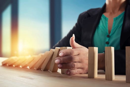 Businesswoman stops a chain fall like domino game toy. Concept of preventing crisis and failure in business