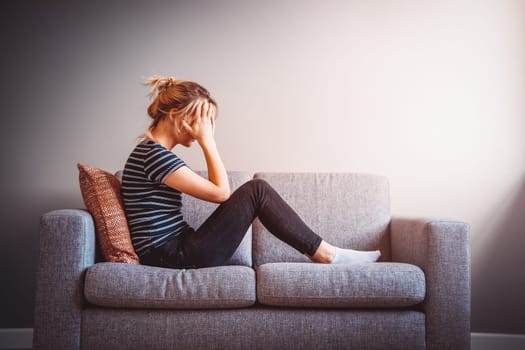 Depressed woman sitting on the couch at home. Concept of the quarantine, job loss and family's problems.