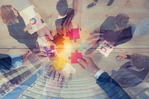 Business people join puzzle pieces over a table in office. Concept of teamwork and partnership. double exposure