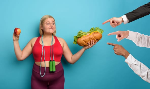 Fat girl is undecided to eat an apple or a big sandwich
