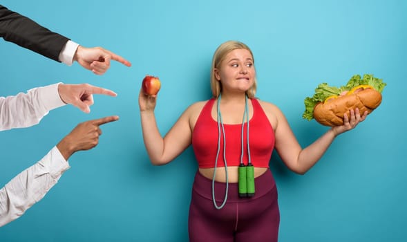 Fat girl is undecided to eat an apple or a big sandwich