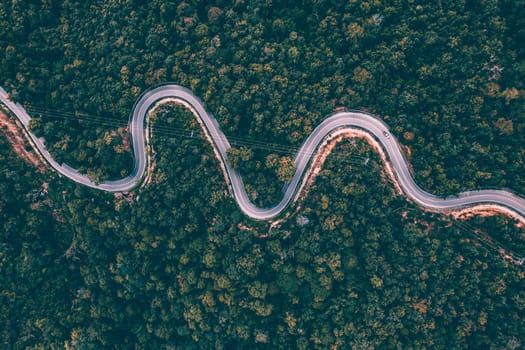 Aerial view of countryside road passing through the green forrest and mountain.