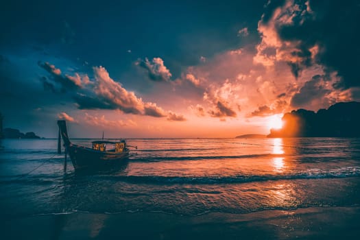 Dramatic sunset over Railay Beach at Krabi, Thailand, with traditional longtail boat in the foreground.