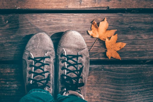 Autumn background of woman shoes over wooden background with autumn leaves.
