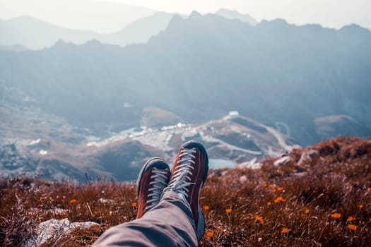 Traveller  legs in trekking boots resting on rock on top of mountain