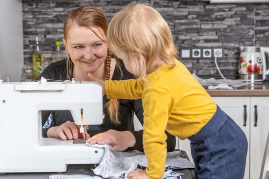 Smiling young mother is sewing with her cute son together. Horizontally.