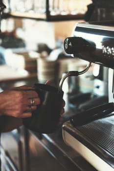 Barista making coffee latte using black pitcher and modern coffee machine and equipment in a coffee shop, pouring milk and mixing to make a cappuccino for clients, concept of restaurant business