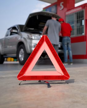 Red triangle reflector roadside warning on the floor. There is a broken pickup car in the background.