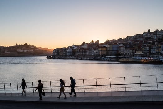 Silhouette family of four who walking along avenue with views over River Douro and Porto cityscape at sunset.