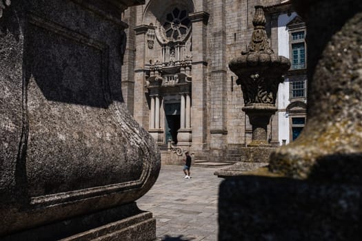 A man with protective face mask walks past the Sé do Porto (Porto Cathedral),  a building of Roman-Gothic structure built in the twelfth century and located in the oldest part of town. Shot taken from the side terrace, next to the medieval pillory of Porto.