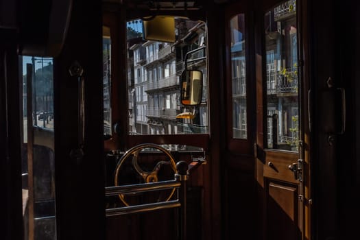 Interior of the rear cabin of one of Porto's historic trams still in service on line 1 and a fascinating view at the typical Portuguese facades through the windows. Retro charme of the design with wooden structure and bronze steering wheel.