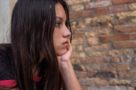 Portrait of beautiful brown hair girl holding chin with hand thinking about emotional problems and looking away, profile view, copy space.