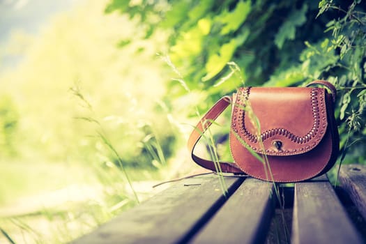 Leather hand bag lies on a wooden park bench, summer time, nobody