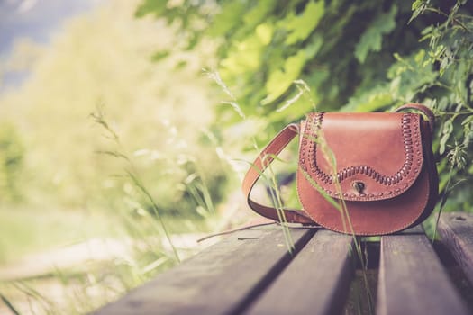 Leather hand bag lies on a wooden park bench, summer time, nobody