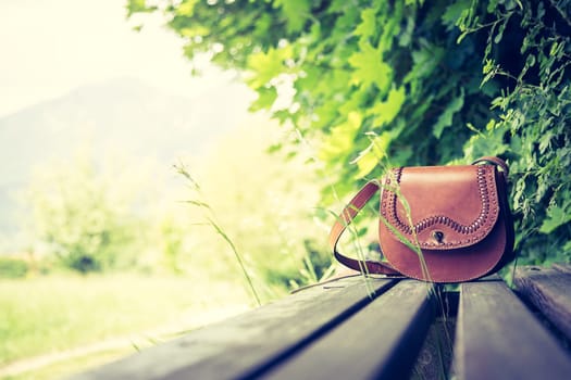 Leather hand bag lies on a wooden park bench, summer time, nobody