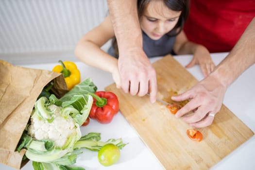 Little girl and her father slicing lemons, tomatoes, and bell peppers on cutting board. Male hands and young child cutting vegetables on wooden board. Daughter-father cooking together