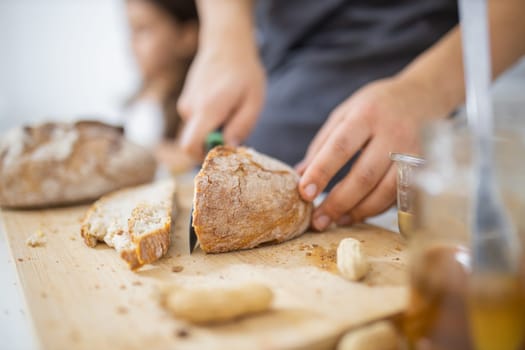 Female hands slicing bread on wooden cutting board. Woman cutting sourdough bread next to honey jar. Healthy meal preparation