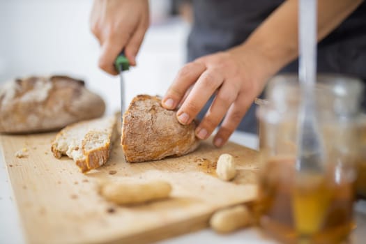 Female hands slicing bread on wooden cutting board. Woman cutting sourdough bread next to honey jar. Healthy meal preparation