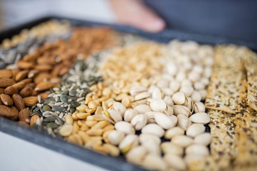 Male hands holding black tray of chickpeas, almonds, peanuts, pistachios, and multi-seed crispbread. Fresh crispy bread, seeds, and nuts. Healthy snacks