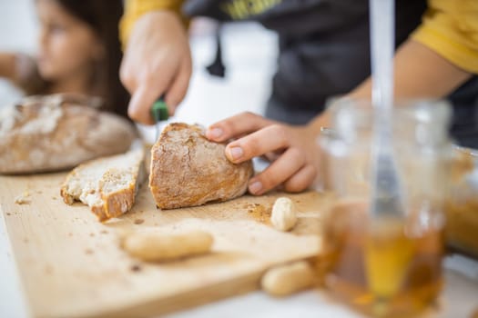 Female hands slicing bread on wooden cutting board. Woman cutting sourdough bread next to honey jar. Healthy meal preparation