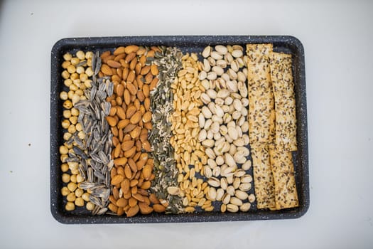 Black tray of chickpeas, almonds, peanuts, pistachios, and multi-seed crispbread. Fresh crispy bread, seeds, and nuts from above. Healthy snacks