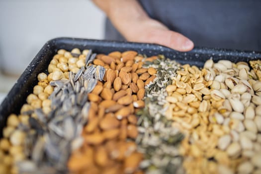 Male hands holding black tray of chickpeas, almonds, peanuts, pistachios, and multi-seed crispbread. Fresh crispy bread, seeds, and nuts. Healthy snacks