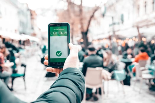 Vaccinated person using immunization certificate on smartphone at the restaurant or terrace.