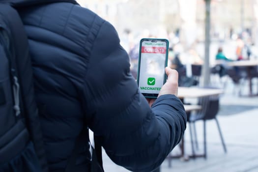 Vaccinated person using immunization certificate on smartphone at the restaurant or terrace.