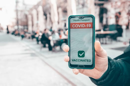 Vaccinated person using immunization certificate on smartphone at the restaurant or terrace.