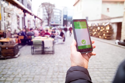 Vaccinated person using immunization certificate on smartphone at the restaurant or terrace.