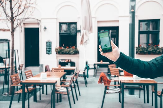 Vaccinated person using immunization certificate on smartphone at the restaurant or terrace.