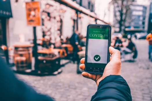 Vaccinated person using immunization certificate on smartphone at the restaurant or terrace.