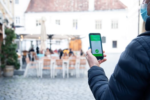 Vaccinated person using immunization certificate on smartphone at the restaurant or terrace.