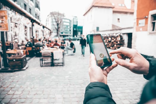 Vaccinated person using immunization certificate on smartphone at the restaurant or terrace.
