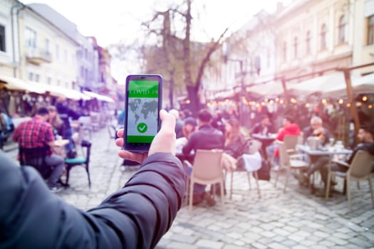 Vaccinated person using immunization certificate on smartphone at the restaurant or terrace.