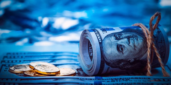 Stacks of coins and a roll of dollars against a background of hundred-dollar bills are scattered throughout the space. The coins are shiny, golden in color.