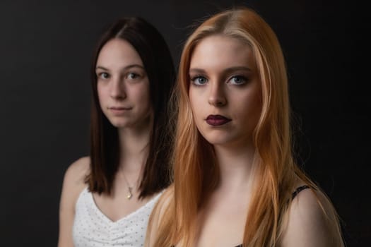 Pair of serious young women is posing on the black background. Horizontally.