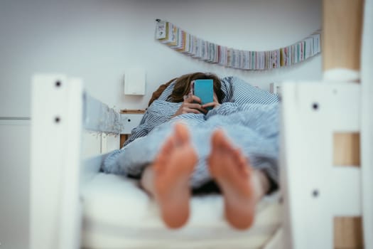 Girl lying in bed is using her smartphone, smartphone in the foreground, blurry background