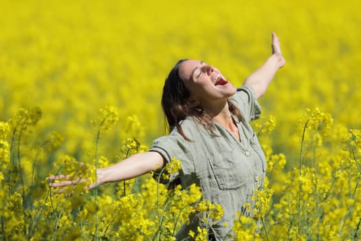 Excited woman celebrating vacation spreading and screaming in a yellow flowered field