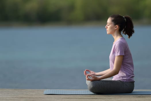 Profile of a yogi practicing yoga in a pier beside a lake
