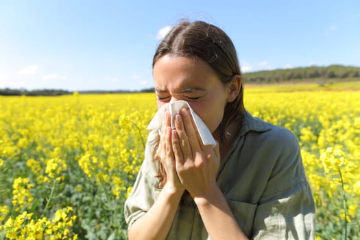 Woman suffering allergy coughing in a yellow flowered field in spring season